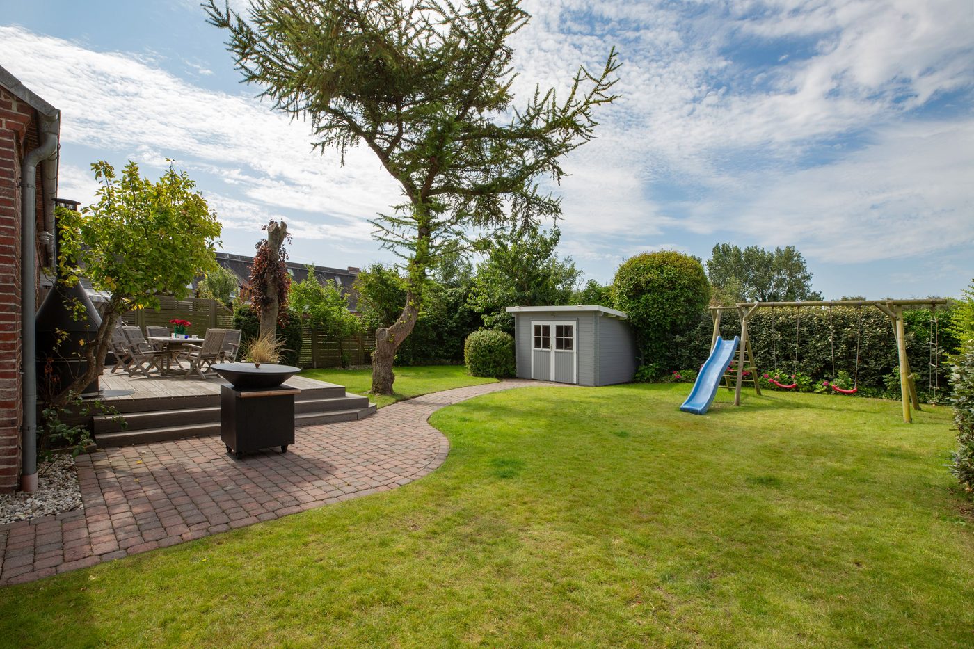 Eingezäunter Garten mit Rasen, Rutsche, Gartenschuppen und Terrasse